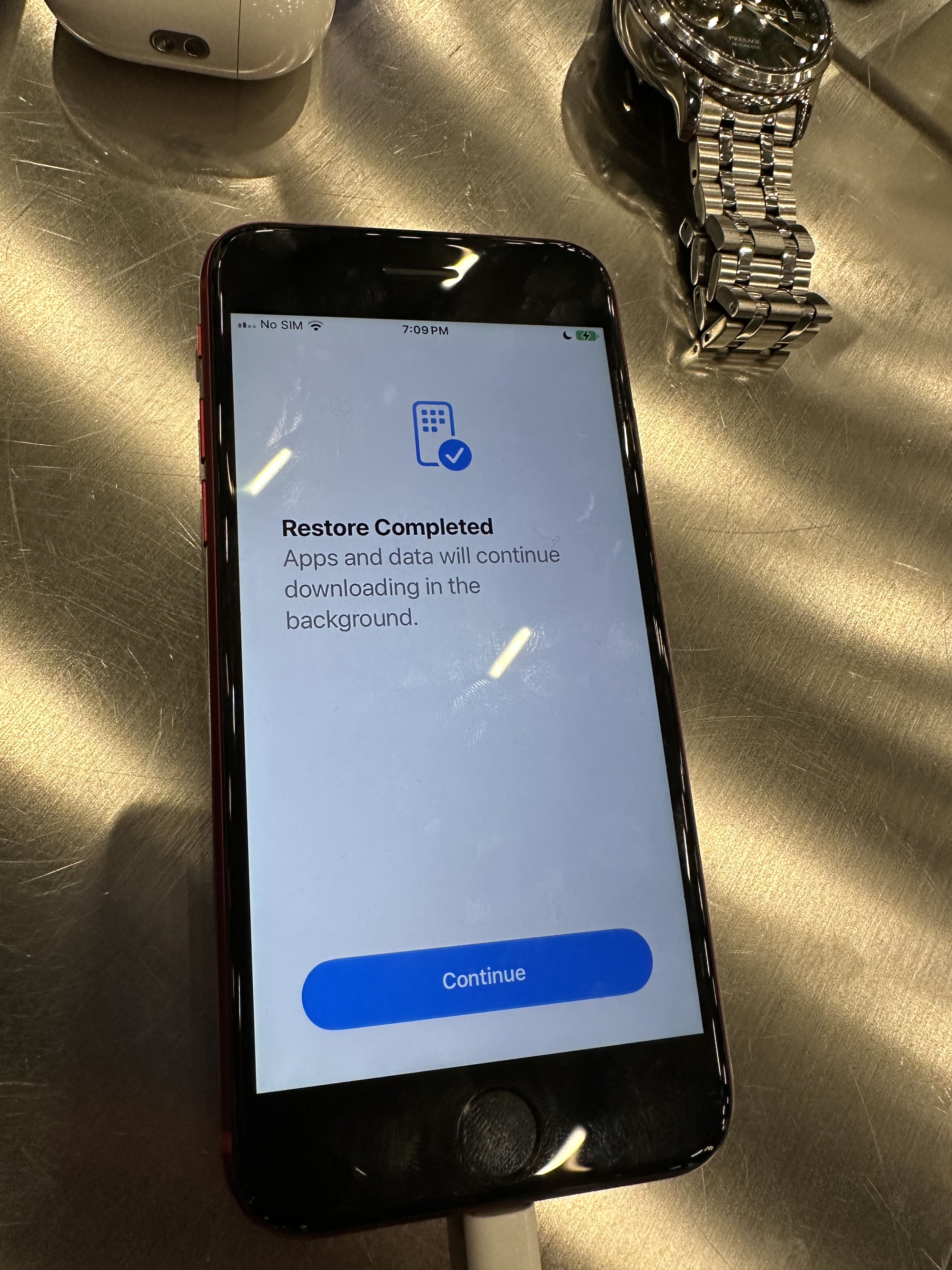 My iPhone SE on the Restore Completed screen with a Continue button, connected to the Mac by cable